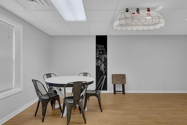 dining space featuring a paneled ceiling, light wood-style floors, and baseboards