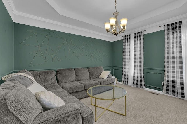 living room featuring a chandelier, carpet flooring, a tray ceiling, a decorative wall, and ornamental molding
