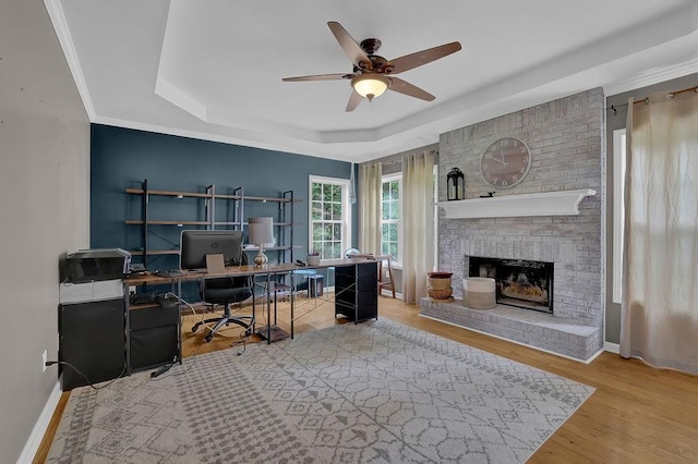 office with a tray ceiling, ceiling fan, a brick fireplace, wood finished floors, and baseboards