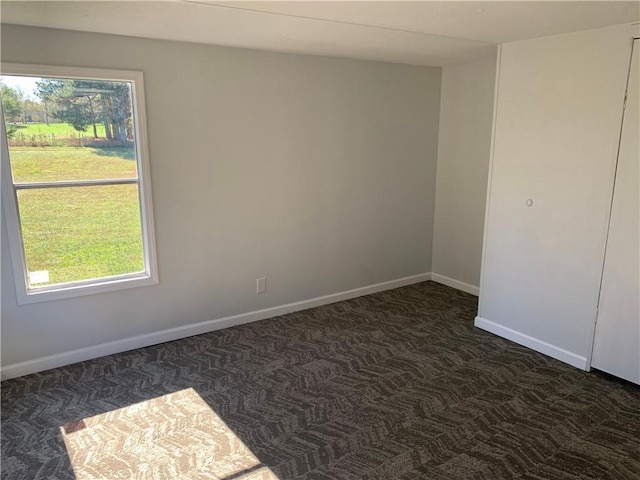 unfurnished room with dark colored carpet and a wealth of natural light