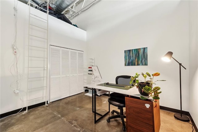 office space featuring a towering ceiling and concrete flooring