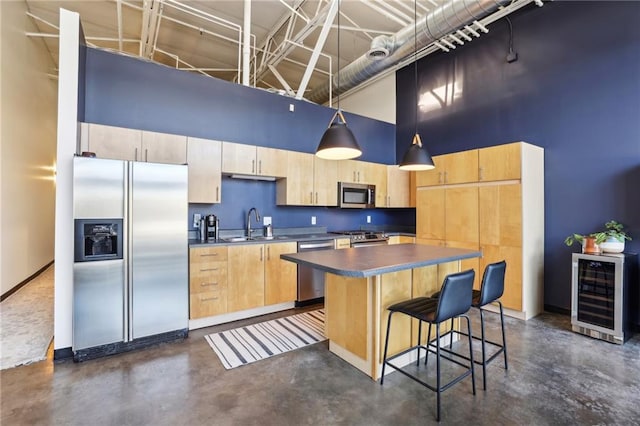 kitchen with a kitchen island, beverage cooler, hanging light fixtures, a high ceiling, and appliances with stainless steel finishes