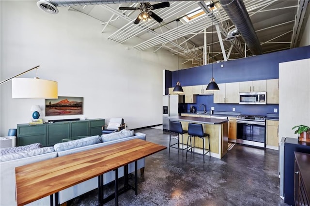 kitchen with stainless steel appliances, a skylight, decorative light fixtures, and a towering ceiling