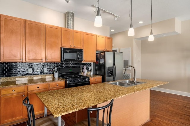 kitchen with hanging light fixtures, a center island with sink, black appliances, a kitchen bar, and sink