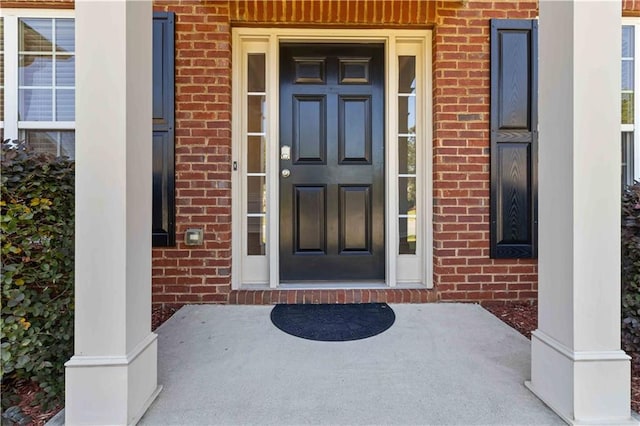 view of exterior entry featuring brick siding and covered porch