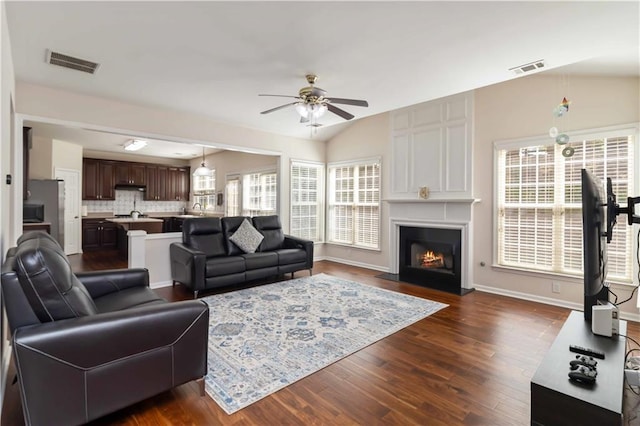 living room with a ceiling fan, dark wood finished floors, a lit fireplace, vaulted ceiling, and baseboards