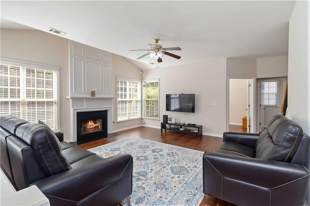 living room with a ceiling fan, dark wood finished floors, vaulted ceiling, a lit fireplace, and baseboards