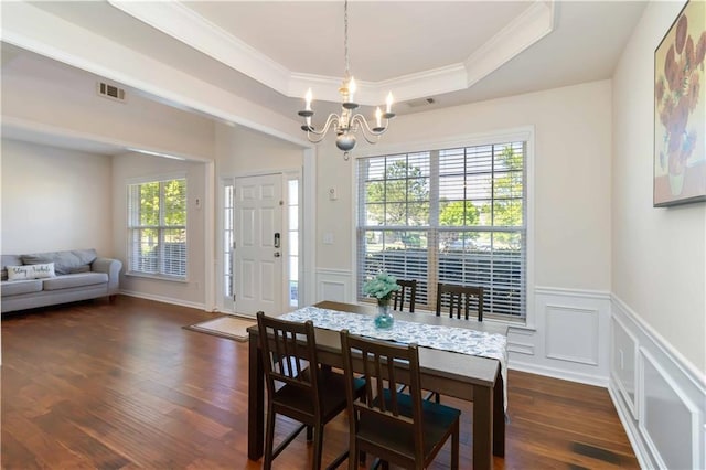 dining area with a chandelier, a raised ceiling, ornamental molding, dark wood-style floors, and a decorative wall