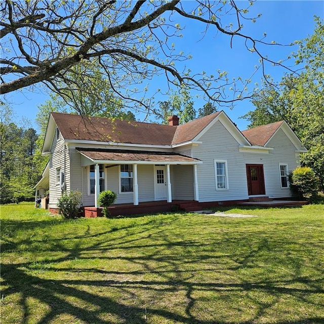 view of front facade with covered porch, a chimney, and a front yard