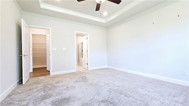 unfurnished bedroom with light carpet, a tray ceiling, ceiling fan, and ensuite bathroom