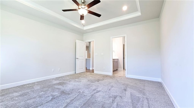 unfurnished bedroom with light carpet, ensuite bath, a raised ceiling, and ceiling fan