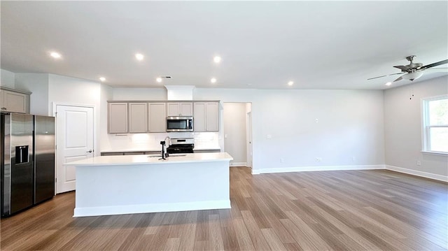 kitchen with sink, gray cabinetry, light wood-type flooring, appliances with stainless steel finishes, and a kitchen island with sink