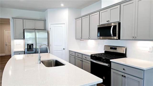 kitchen with sink, stainless steel appliances, tasteful backsplash, light stone countertops, and a center island with sink