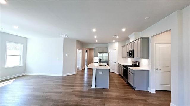 kitchen featuring dark wood-type flooring, sink, gray cabinetry, an island with sink, and stainless steel appliances