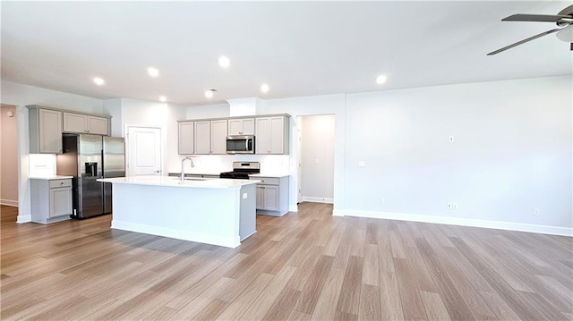 kitchen featuring a kitchen island with sink, light wood-type flooring, gray cabinets, and appliances with stainless steel finishes