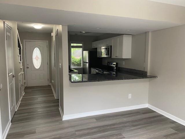 kitchen featuring dark wood-type flooring, white cabinetry, stainless steel appliances, kitchen peninsula, and dark stone counters