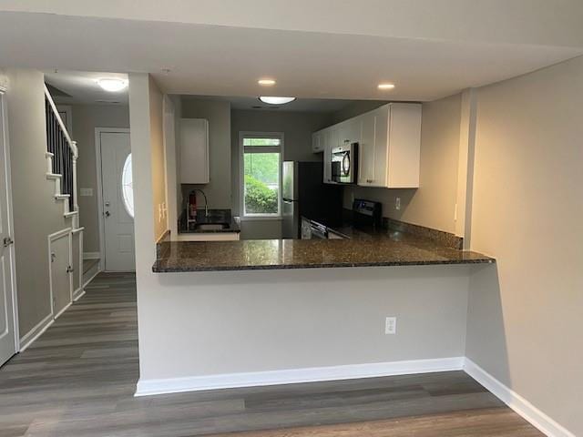 kitchen featuring dark wood-type flooring, white cabinetry, stainless steel appliances, kitchen peninsula, and dark stone counters