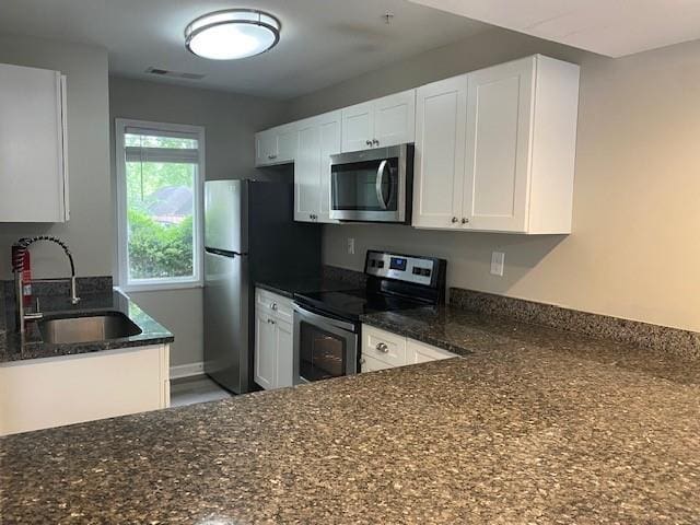 kitchen featuring stainless steel appliances, sink, dark stone counters, and white cabinets