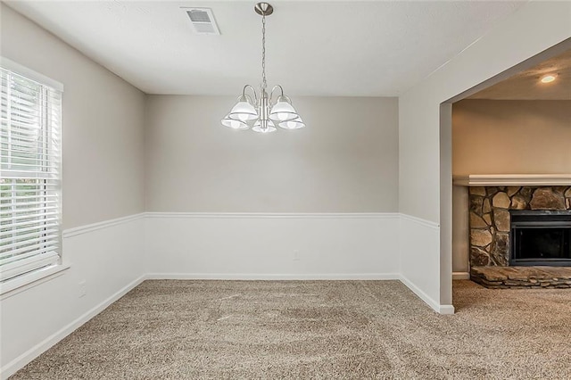 unfurnished dining area with carpet, baseboards, a chandelier, and a stone fireplace