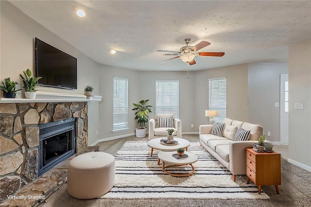 carpeted living room featuring baseboards, a stone fireplace, a ceiling fan, healthy amount of natural light, and a textured ceiling
