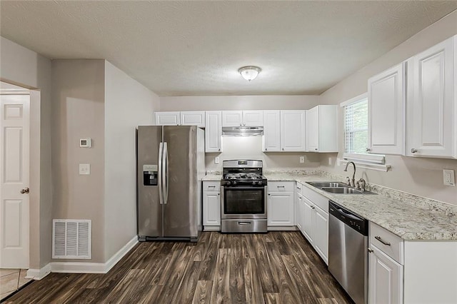kitchen featuring stainless steel appliances, a sink, under cabinet range hood, dark wood-type flooring, and white cabinetry