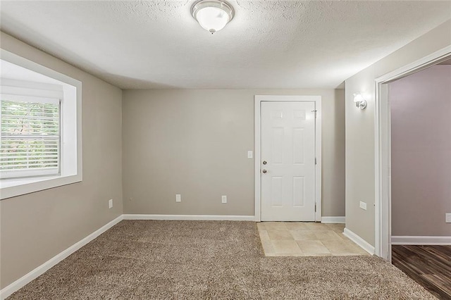unfurnished room with light colored carpet, baseboards, and a textured ceiling