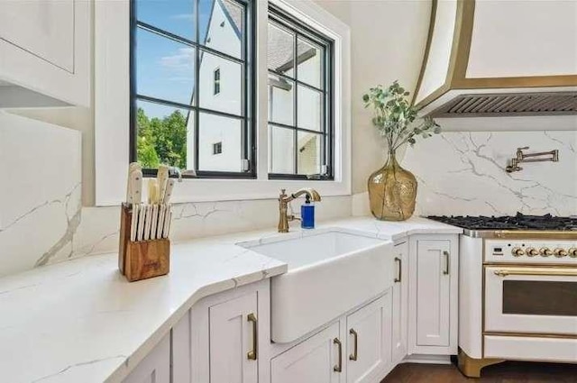 kitchen featuring a sink, white cabinets, oven, tasteful backsplash, and light stone counters