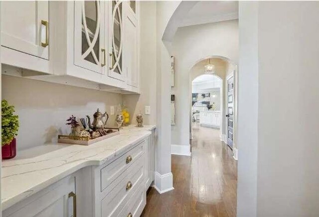 hall featuring arched walkways, dark wood-type flooring, and baseboards