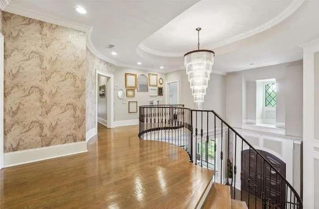 corridor featuring an upstairs landing, crown molding, a chandelier, wallpapered walls, and wood finished floors