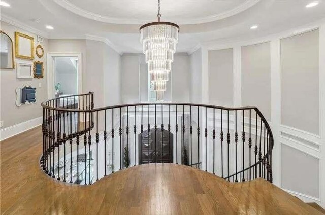 stairway featuring a chandelier, ornamental molding, wood finished floors, recessed lighting, and a raised ceiling