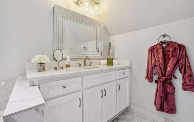 bathroom with marble finish floors, vanity, and vaulted ceiling