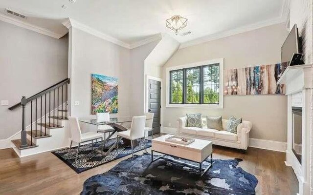 living area with crown molding, wood finished floors, stairs, baseboards, and a fireplace