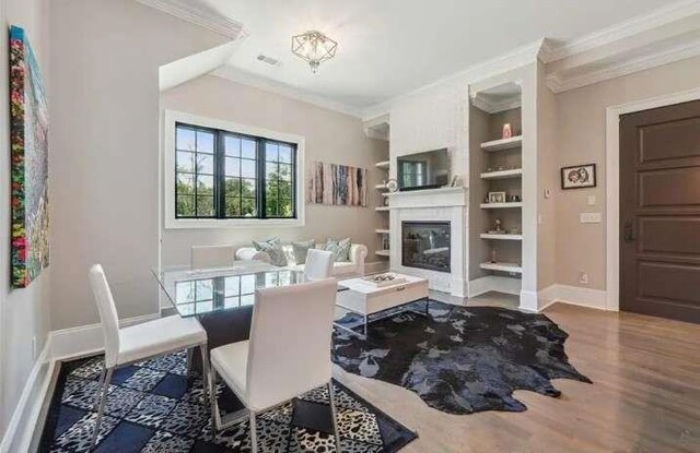 living room with ornamental molding, wood finished floors, a glass covered fireplace, built in features, and baseboards