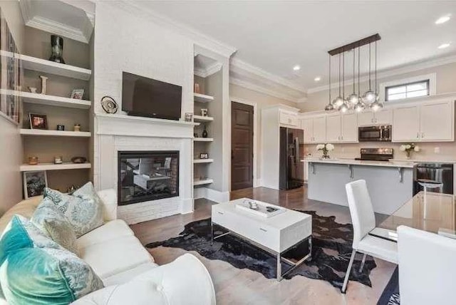 living room featuring crown molding, a glass covered fireplace, built in shelves, recessed lighting, and dark wood-style floors