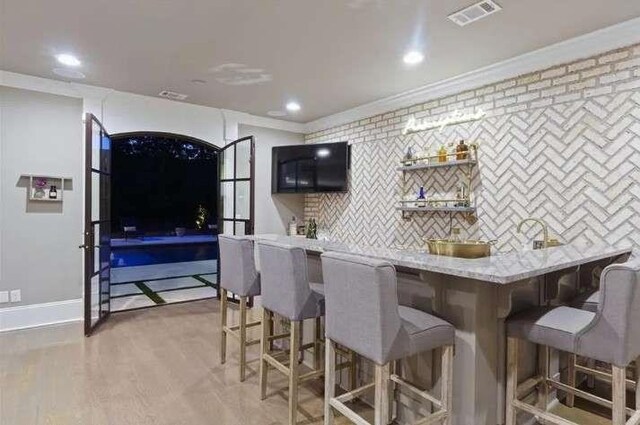 kitchen with crown molding, a breakfast bar area, recessed lighting, backsplash, and light wood-style floors