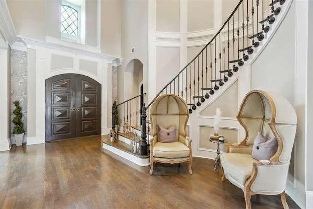 entryway with a high ceiling, stairway, wood finished floors, and arched walkways