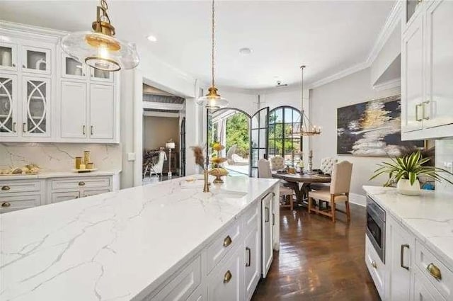 kitchen featuring white cabinets, decorative light fixtures, glass insert cabinets, light stone counters, and ornamental molding