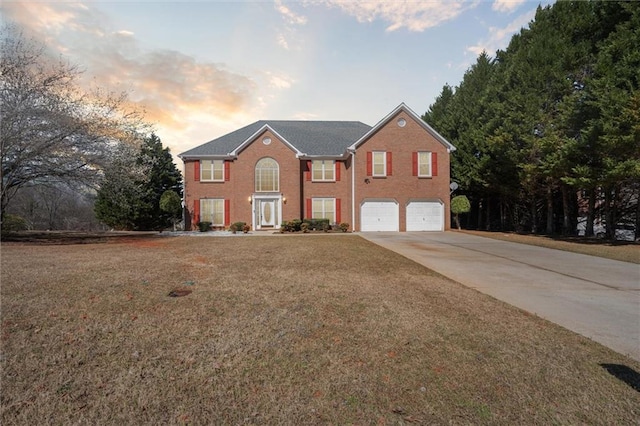 colonial inspired home with brick siding, an attached garage, driveway, and a front yard