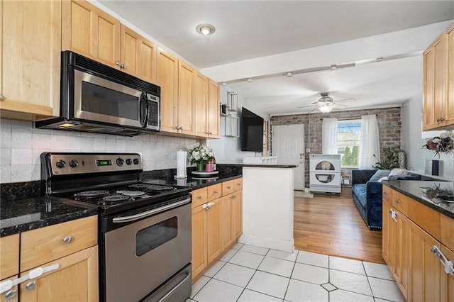 kitchen with appliances with stainless steel finishes, ceiling fan, dark stone countertops, and light tile patterned flooring