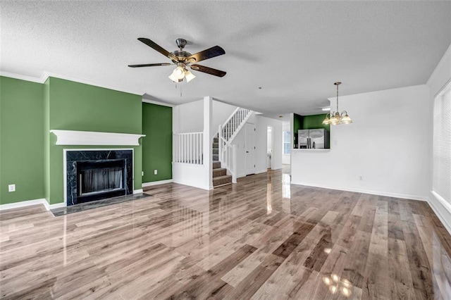 unfurnished living room with a high end fireplace, ceiling fan with notable chandelier, crown molding, hardwood / wood-style flooring, and a textured ceiling