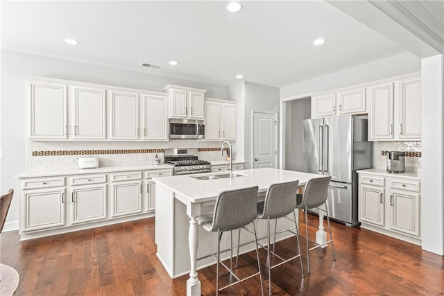 kitchen with a kitchen island with sink, stainless steel appliances, dark wood-type flooring, a sink, and visible vents