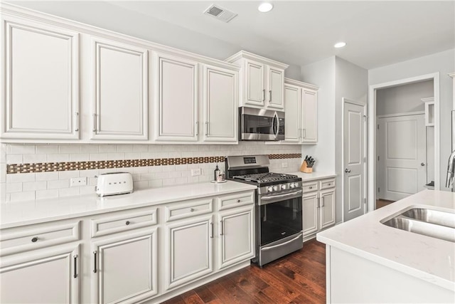 kitchen with dark wood finished floors, stainless steel appliances, light countertops, visible vents, and a sink