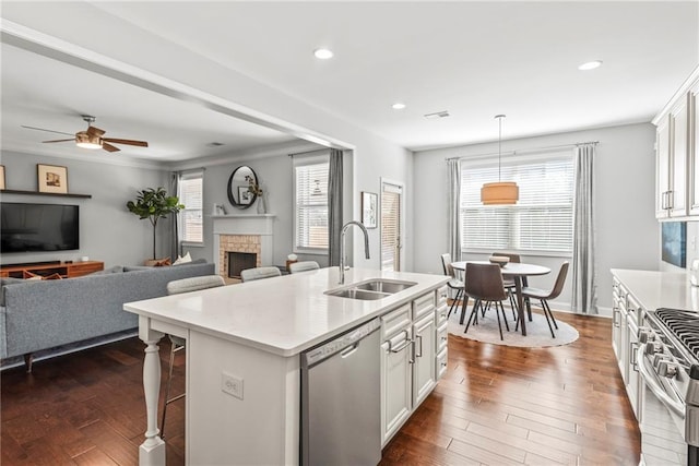 kitchen with stainless steel appliances, light countertops, dark wood-type flooring, a sink, and an island with sink