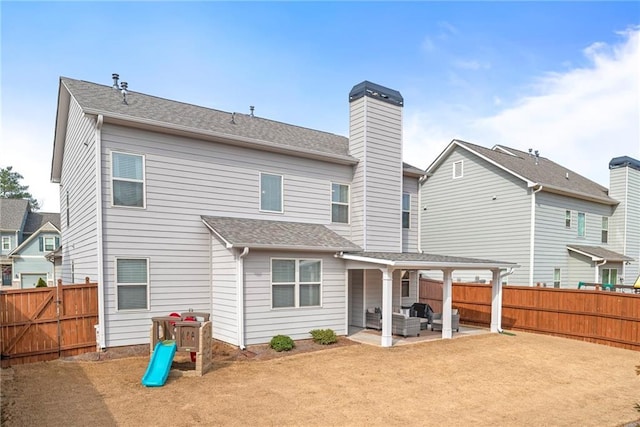 rear view of house featuring a fenced backyard, a chimney, roof with shingles, and a patio