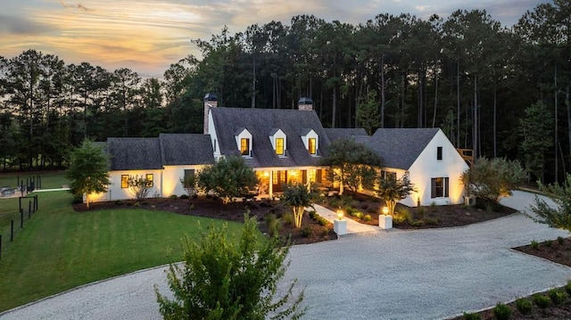 cape cod-style house with a chimney, a front yard, and gravel driveway