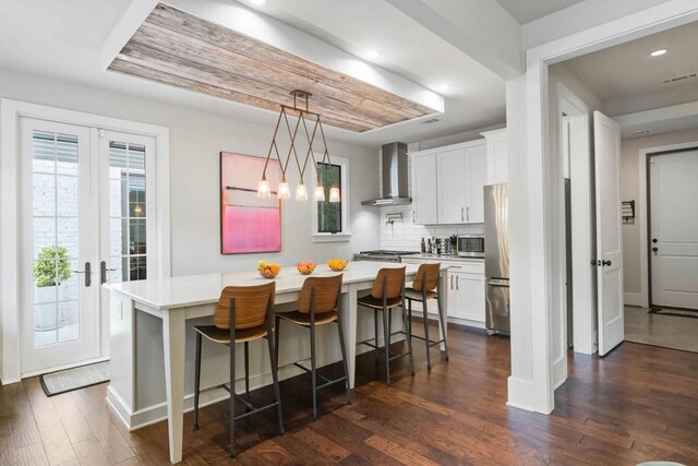 kitchen with wall chimney exhaust hood, appliances with stainless steel finishes, light countertops, a breakfast bar area, and white cabinets