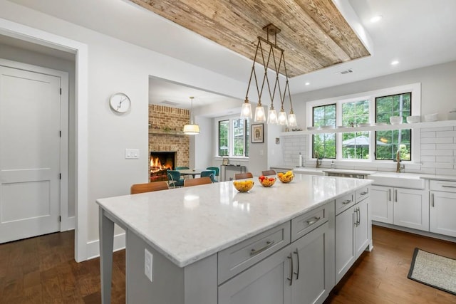 kitchen featuring a sink, a brick fireplace, a center island, light stone counters, and dark wood finished floors