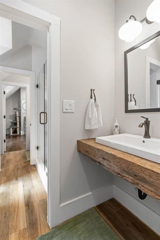 bathroom with wood finished floors, a shower stall, a sink, and baseboards