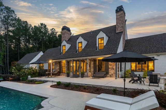 back of house at dusk with a chimney, stone siding, and a patio area