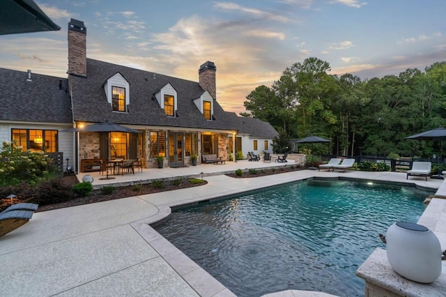 pool at dusk with a patio area, fence, and an outdoor pool